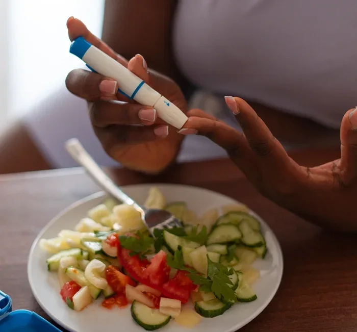 Woman checking her blood sugar beside a plate of fresh salad