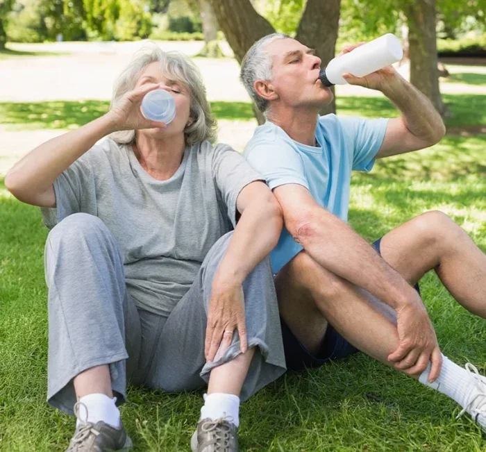 Older couple hydrating together after exercising in the park